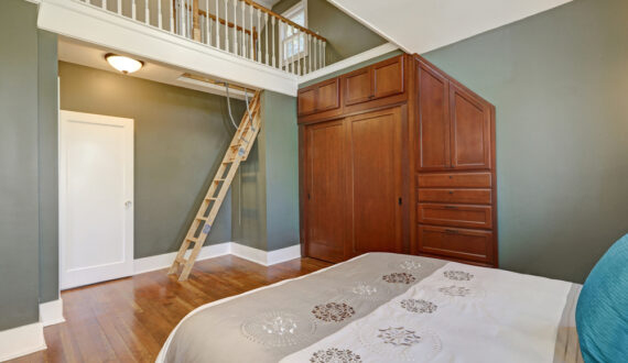 Immagine di una camera da letto realizzata con mobili su misura, quali: letto, armadio e scala in legno.